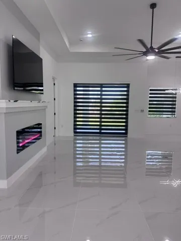 Unfurnished living room featuring a ceiling fan and a tray ceiling