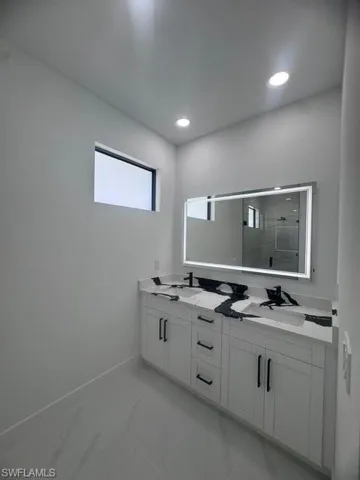 Full bath featuring double vanity, a stall shower, recessed lighting, and marble look tile flooring