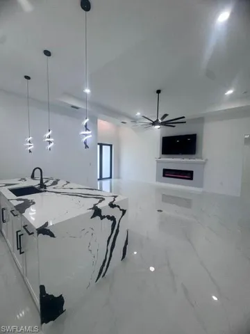Kitchen featuring white cabinets, a lit fireplace, light stone countertops, light marble finish floors, and decorative light fixtures