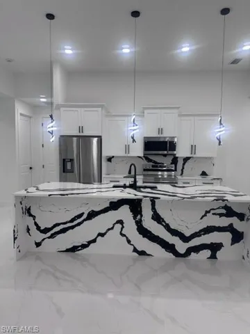 Kitchen featuring marble finish flooring, refrigerator, white stove, and decorative light fixtures