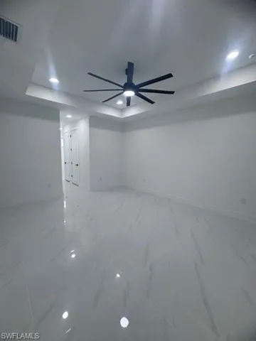 Spare room with recessed lighting, a ceiling fan, a raised ceiling, and light marble finish flooring