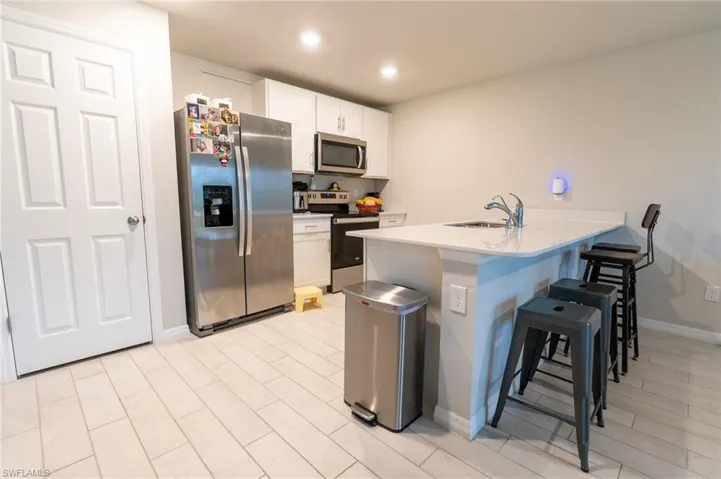 Kitchen with a kitchen bar, white cabinetry, appliances with stainless steel finishes, and sink