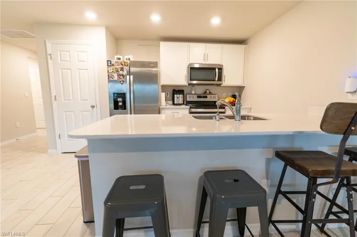 Kitchen with a breakfast bar, light hardwood / wood-style floors, sink, white cabinets, and appliances with stainless steel finishes