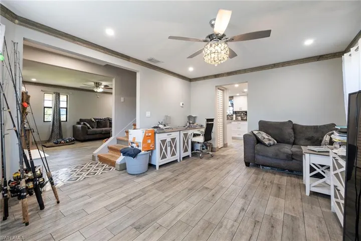 Living area featuring a ceiling fan, light wood finished floors, crown molding, recessed lighting, and stairway