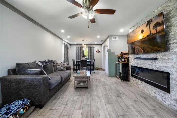Living area featuring light wood-type flooring, a ceiling fan, recessed lighting, a stone fireplace, and crown molding