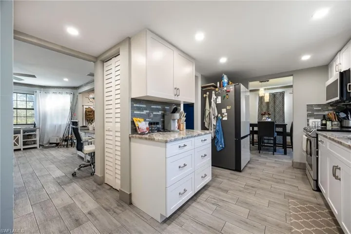 Kitchen with stainless steel appliances, decorative backsplash, light wood finished floors, white cabinets, and light stone countertops