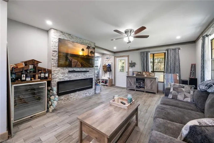 Living area with wine cooler, ornamental molding, wood finished floors, ceiling fan, and a stone fireplace