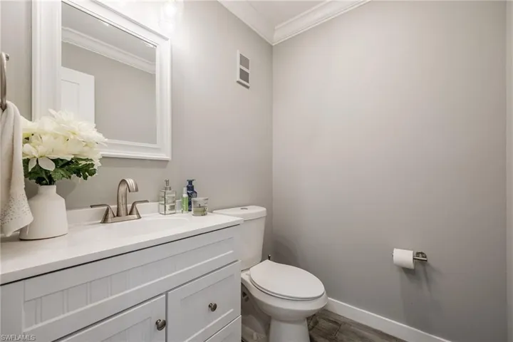 Bathroom with ornamental molding, toilet, vanity, wood finished floors, and baseboards
