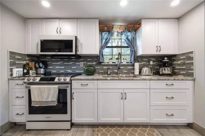 Kitchen with white microwave, stainless steel electric stove, a sink, white cabinetry, and light wood finished floors