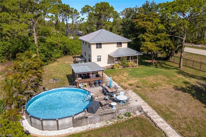 Back of property with a deck, an outdoor pool, metal roof, and view of wooded area