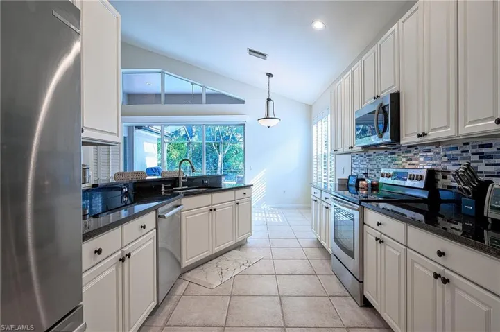 Kitchen featuring stainless steel appliances, vaulted ceiling, sink, tasteful backsplash, and white cabinetry