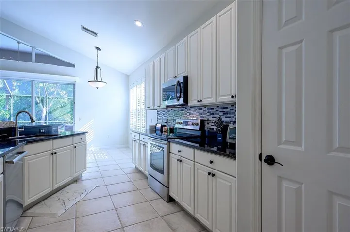 Kitchen featuring appliances with stainless steel finishes, lofted ceiling, and white cabinets