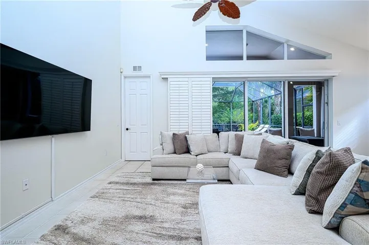 Living room featuring high vaulted ceiling, light tile patterned flooring, and ceiling fan