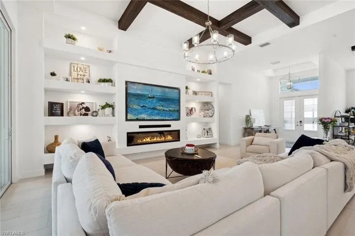 Living room featuring beam ceiling, a notable chandelier, built in features, and french doors