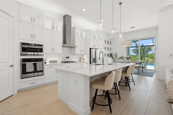 Kitchen featuring stainless steel appliances, a center island with sink, white cabinets, wall chimney range hood, and sink