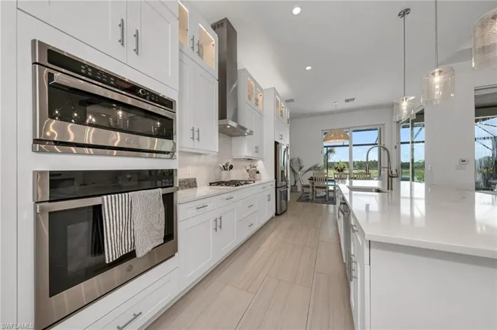Kitchen featuring appliances with stainless steel finishes, sink, a kitchen island with sink, white cabinetry, and wall chimney exhaust hood