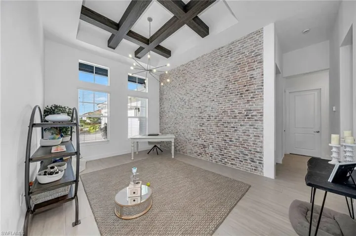 Living room featuring brick wall, light hardwood / wood-style flooring, beam ceiling, a chandelier, and coffered ceiling