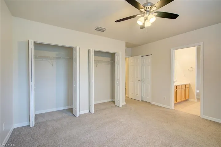 Unfurnished bedroom featuring ensuite bathroom, light carpet, two closets, and ceiling fan
