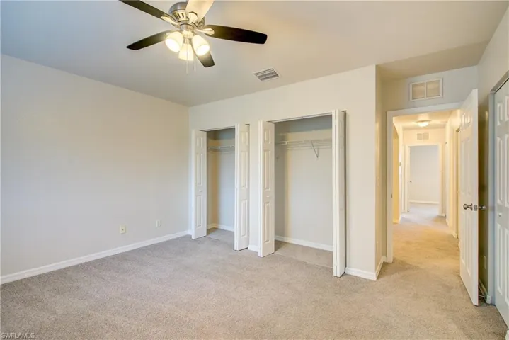 Unfurnished bedroom with two closets, light colored carpet, and ceiling fan