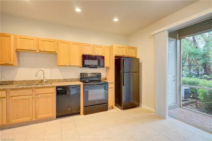 Kitchen featuring sink, light stone counters, black appliances, light tile patterned flooring, and light brown cabinets
