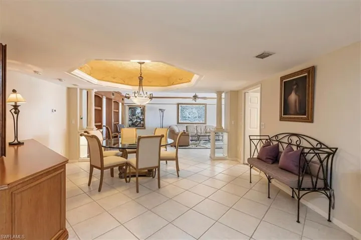 Dining space featuring ornate columns, a raised ceiling, and light tile patterned floors