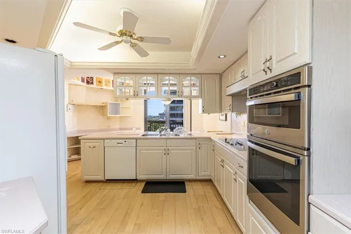 Kitchen with white appliances, light countertops, light wood finished floors, glass insert cabinets, and ceiling fan