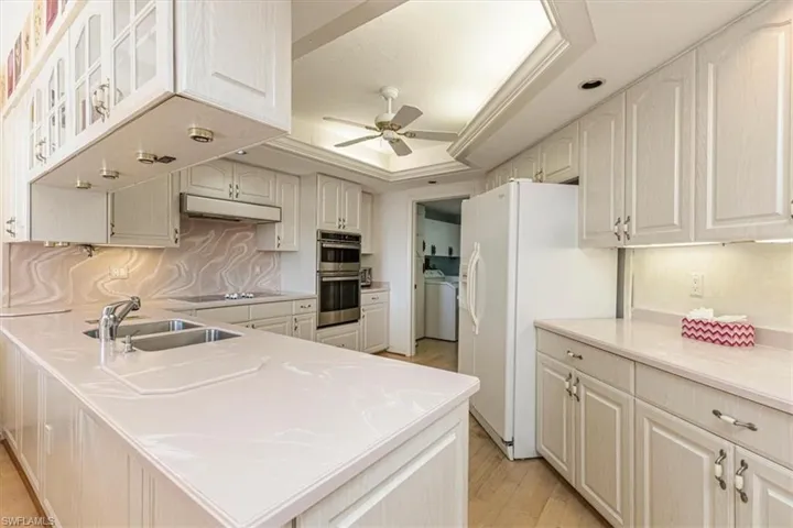 Kitchen with a peninsula, white refrigerator with ice dispenser, light wood-style flooring, a ceiling fan, and a raised ceiling
