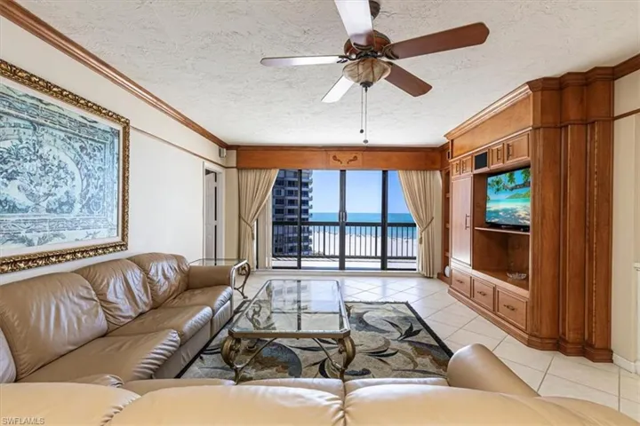 Living area with ceiling fan, a textured ceiling, light tile patterned flooring, and crown molding