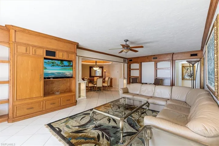 Living room featuring ornamental molding, ceiling fan, light tile patterned floors, and a textured ceiling