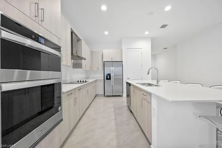 Kitchen with an island with sink, light tile flooring, wall chimney exhaust hood, sink, and appliances with stainless steel finishes