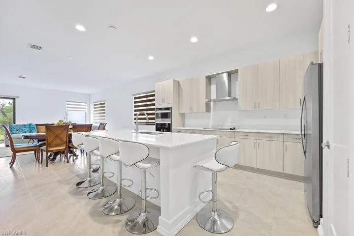 Kitchen with an island with sink, stainless steel appliances, light tile floors, wall chimney exhaust hood, and sink