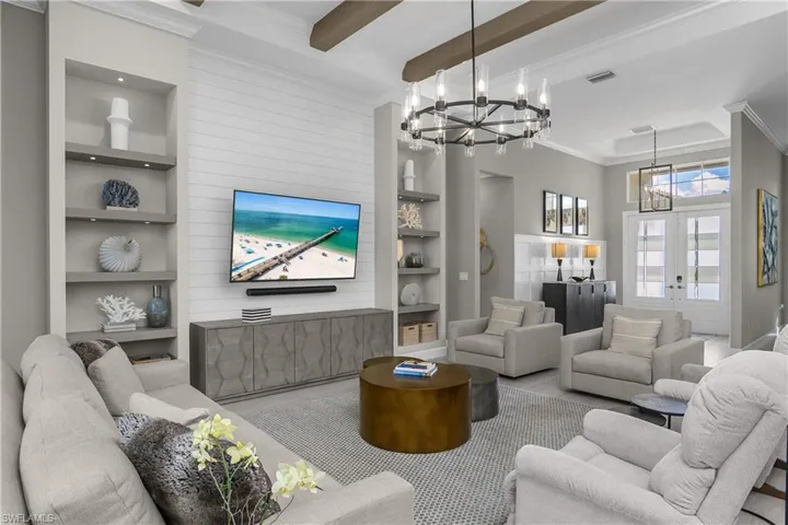 Living room featuring built in shelves, crown molding, beamed ceiling, suspended lighting, and wood finished floors