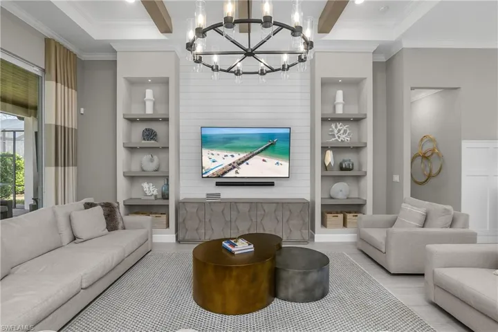 Living room with built in features, crown molding, beam ceiling, hanging lights, and wood finished floors