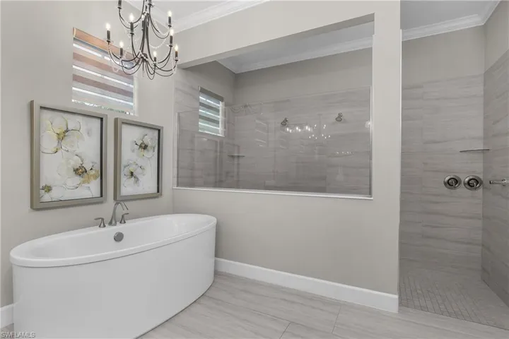 Full bath featuring walk in shower, crown molding, a chandelier, and a soaking tub
