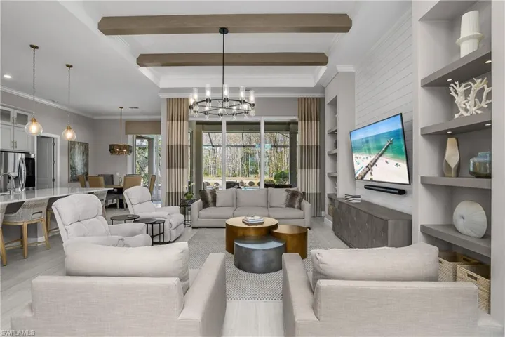Living area with suspended lighting, ornamental molding, built in shelves, wood finished floors, and beamed ceiling