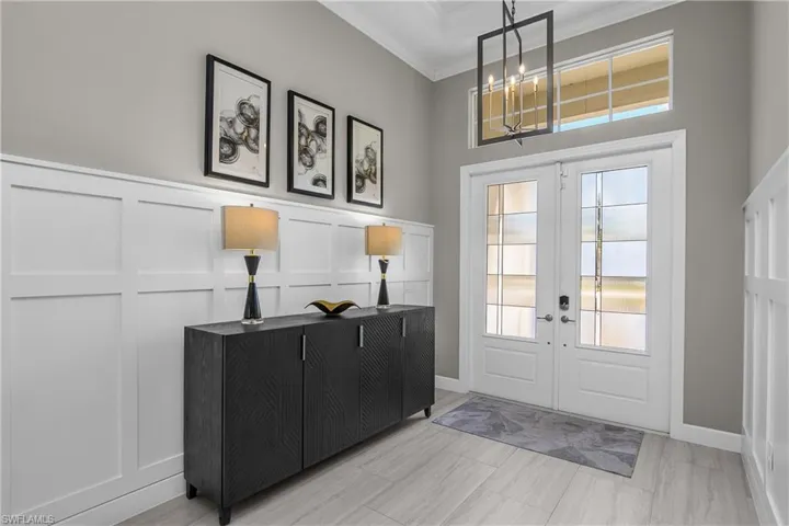 Entryway featuring french doors, a decorative wall, crown molding, and suspended lighting
