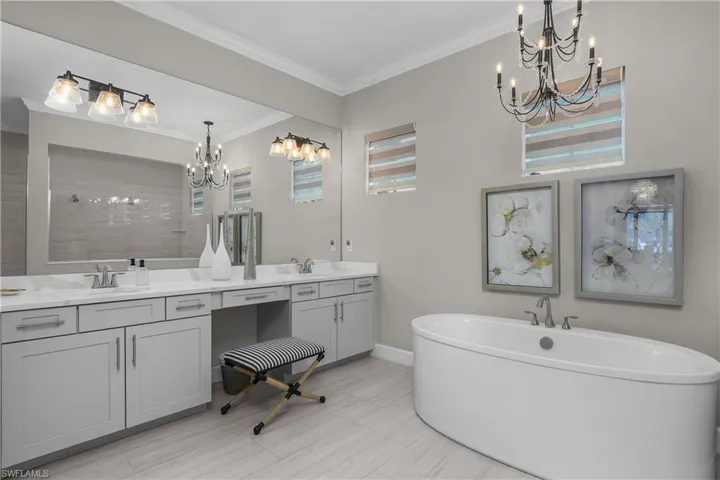 Bathroom with a chandelier, double vanity, a soaking tub, ornamental molding, and tiled shower