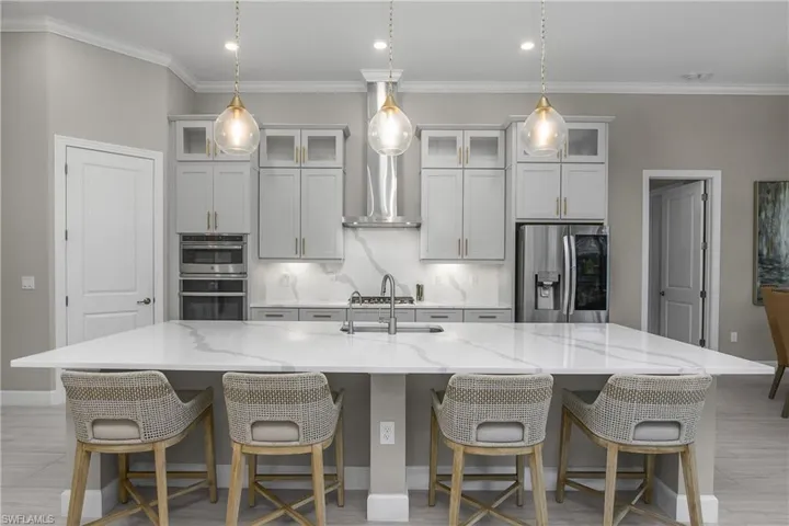 Kitchen with stainless steel appliances, a kitchen breakfast bar, backsplash, light stone counters, and a spacious island