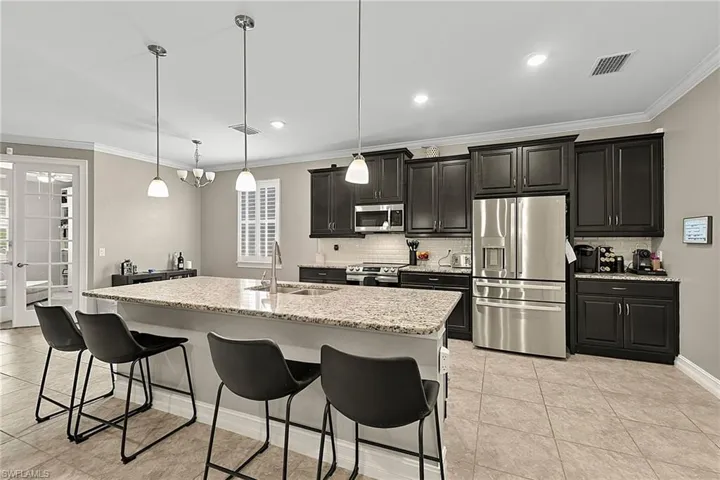 Spacious kitchen featuring a large island with a stone countertop, dark wood cabinetry, stainless steel appliances, and tile flooring