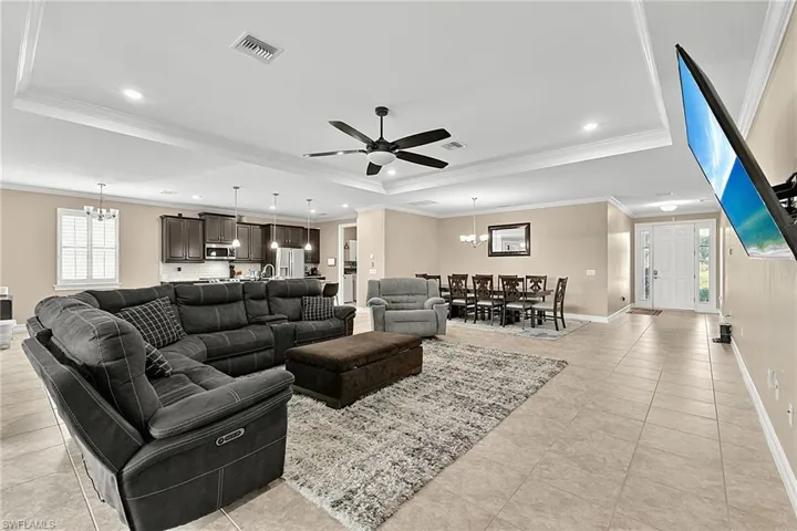 Expansive open-concept living area featuring tray ceilings, recessed lighting, and a ceiling fan