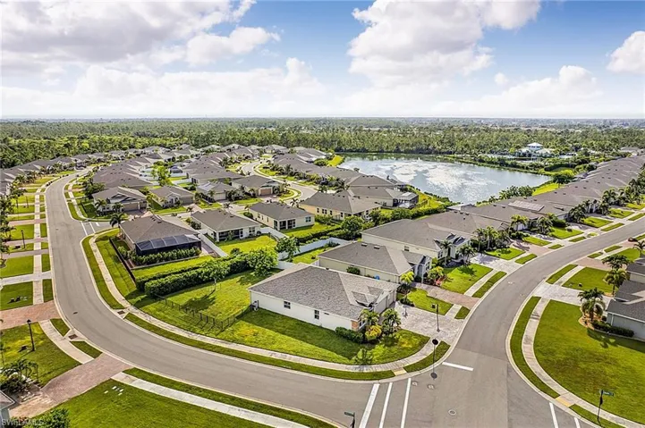 Residential community featuring a curved street design, manicured green spaces, paved sidewalks, and a central pond