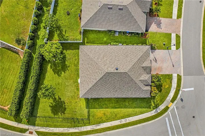 Gable roofline residence featuring a paver driveway, verdant lawn, mature privacy hedges, and a black wrought-iron fence