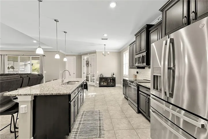 Spacious kitchen featuring an extended island with a sink, pendant lighting, stainless steel appliances, dark wood cabinetry, and a subway tile backsplash