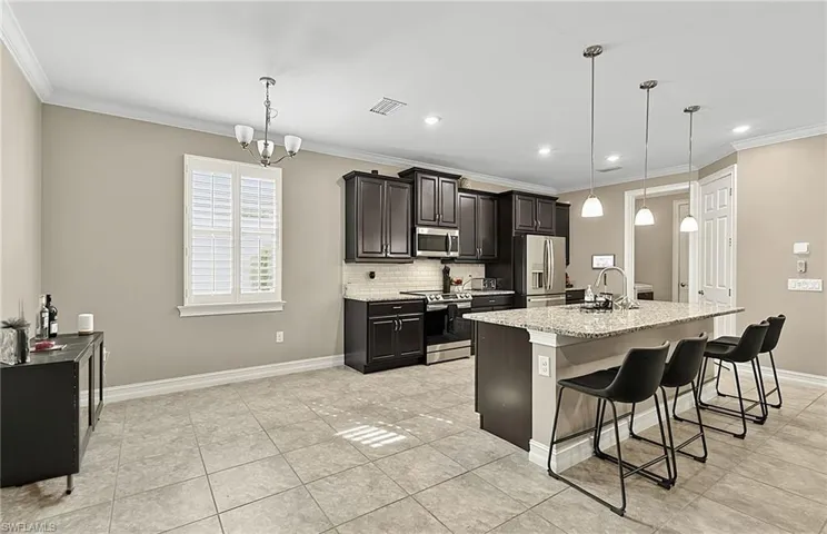 Spacious kitchen and dining area featuring ceramic tile flooring, dark wood cabinetry, stainless steel appliances, a kitchen island with seating, and plantation shutters