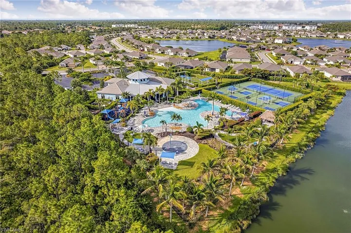 Community amenities featuring a central clubhouse with a circular roofline, a large swimming pool, an adjacent children's play area, and multiple tennis courts