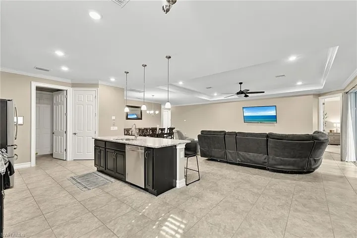 Open-concept living area featuring a central kitchen island with seating, a recessed ceiling with crown molding, a ceiling fan, and tile flooring throughout