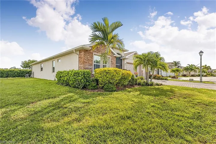 Stucco exterior with stone accent facade, featuring a verdant lawn and mature palm trees