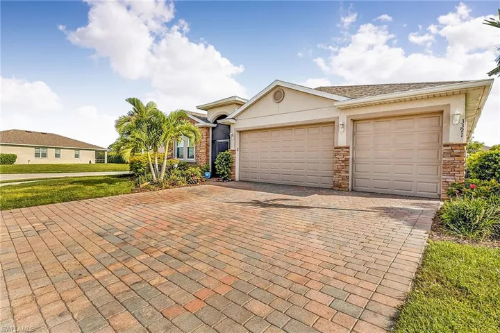 Exterior featuring a three-car garage, stone-accented facade, and a paver driveway