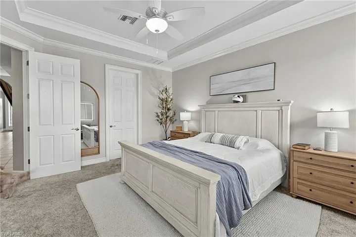Bedroom featuring tray ceilings with crown molding, a ceiling fan with integrated lighting, and neutral carpeting