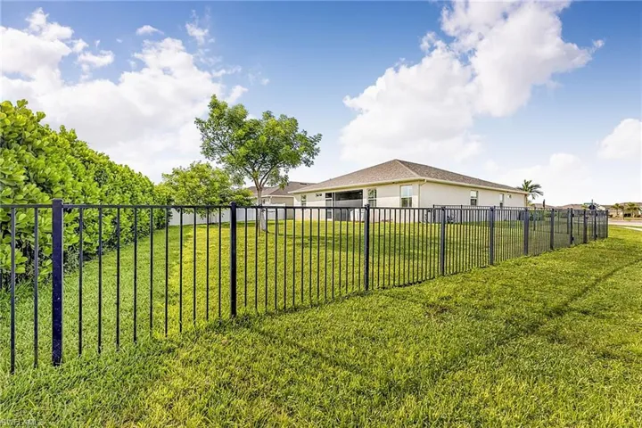 Expansive backyard featuring a black metal perimeter fence, established lawn, and mature trees